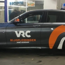 Side View Of A Grey BMW With A RIJOPLEIDINGEN Orange / White Branding, Silver Alloy Wheels & Orange AlloyGator Wheel Protection With Match The Orange Brand Colour.